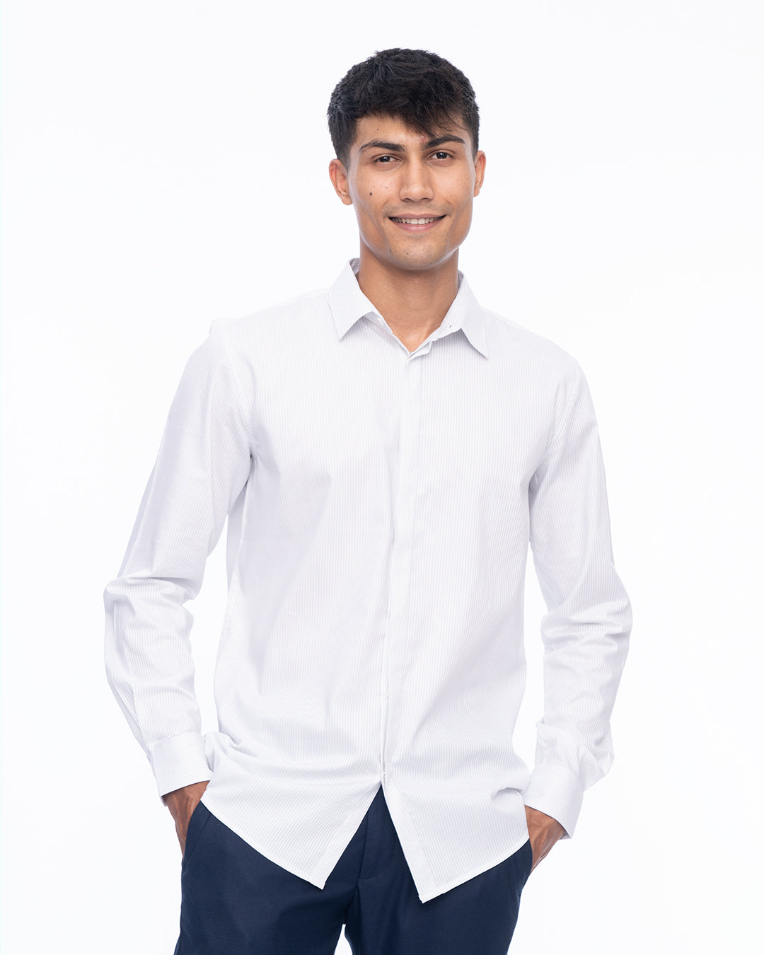 A young man stands against a plain white background, smiling and wearing a Sky Line - Classic Shirt made from premium cotton paired with dark pants. His hands are relaxed and resting in his pockets.