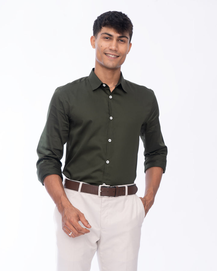 A man is standing against a plain white background, wearing an Emerald - Classic Shirt with white buttons and light-colored pants. He is smiling and looking to his left, with his hands slightly clasped in front of him.